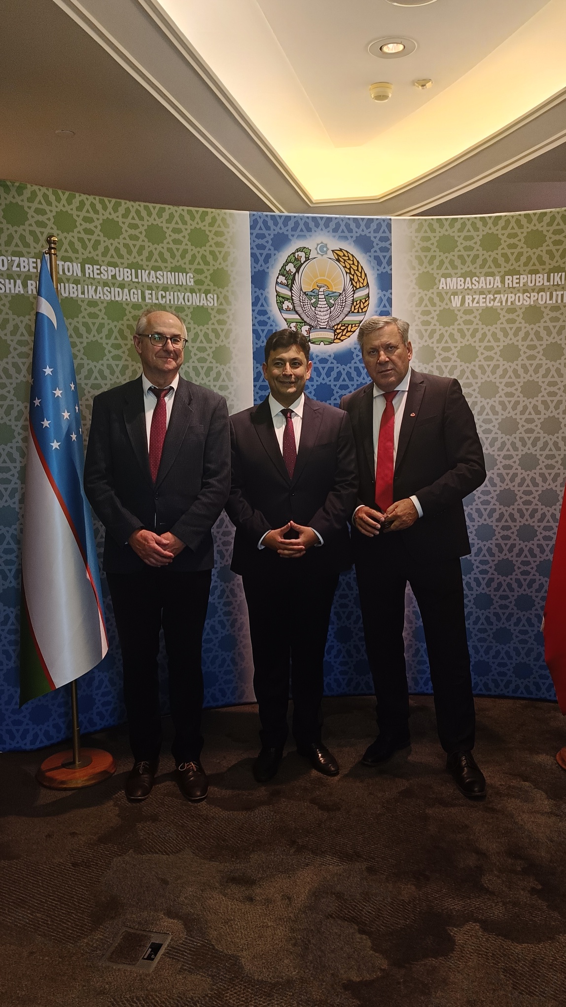 Dr Szukalski i dwóch innych mężczyzn stojących na tle godła Uzbekistanu