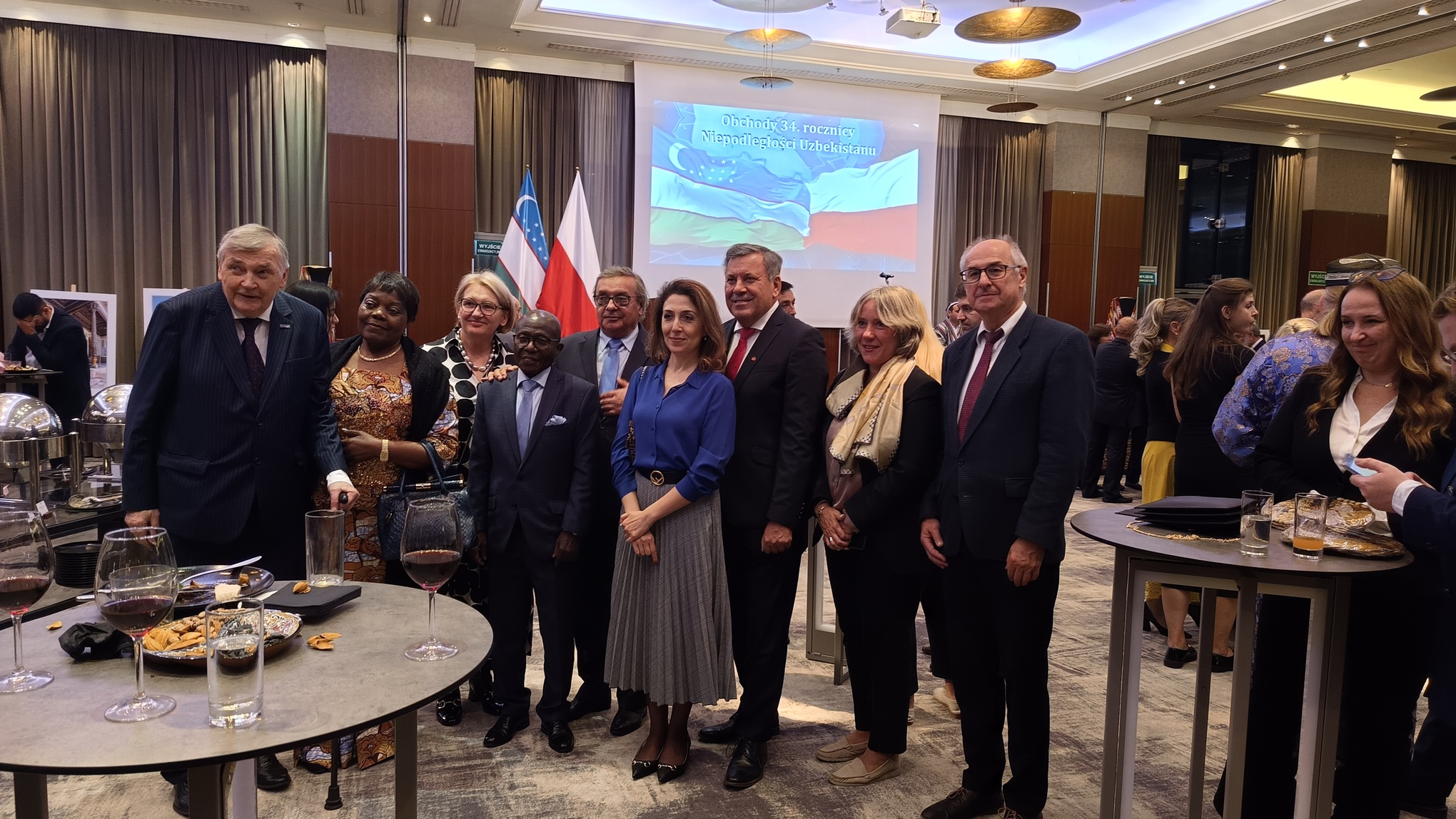 Grupa stojących osób na tle flag Polski i Uzbekistanu