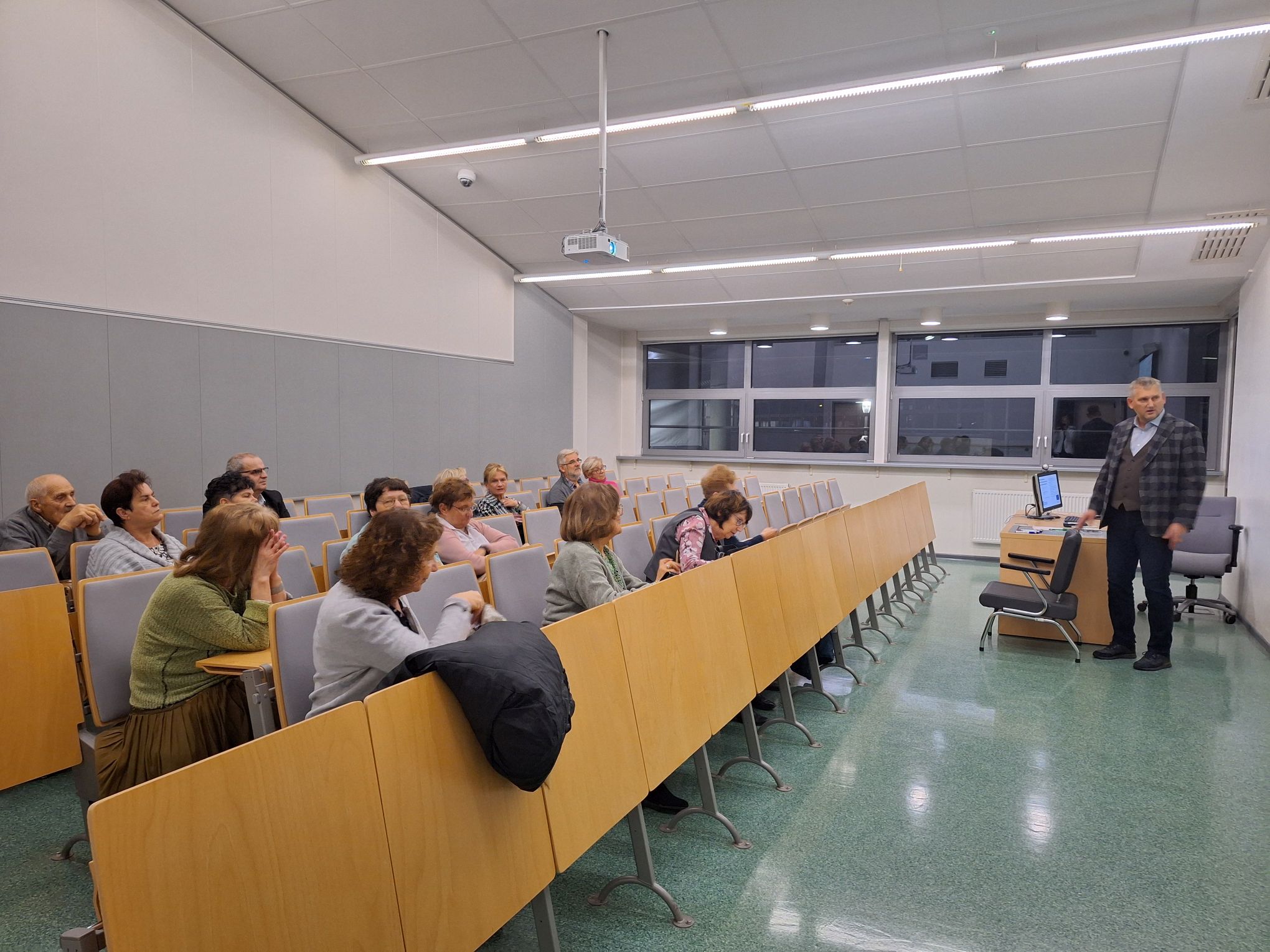 The photo shows Prof. Indraszczyk standing and the audience sitting at the lecture.