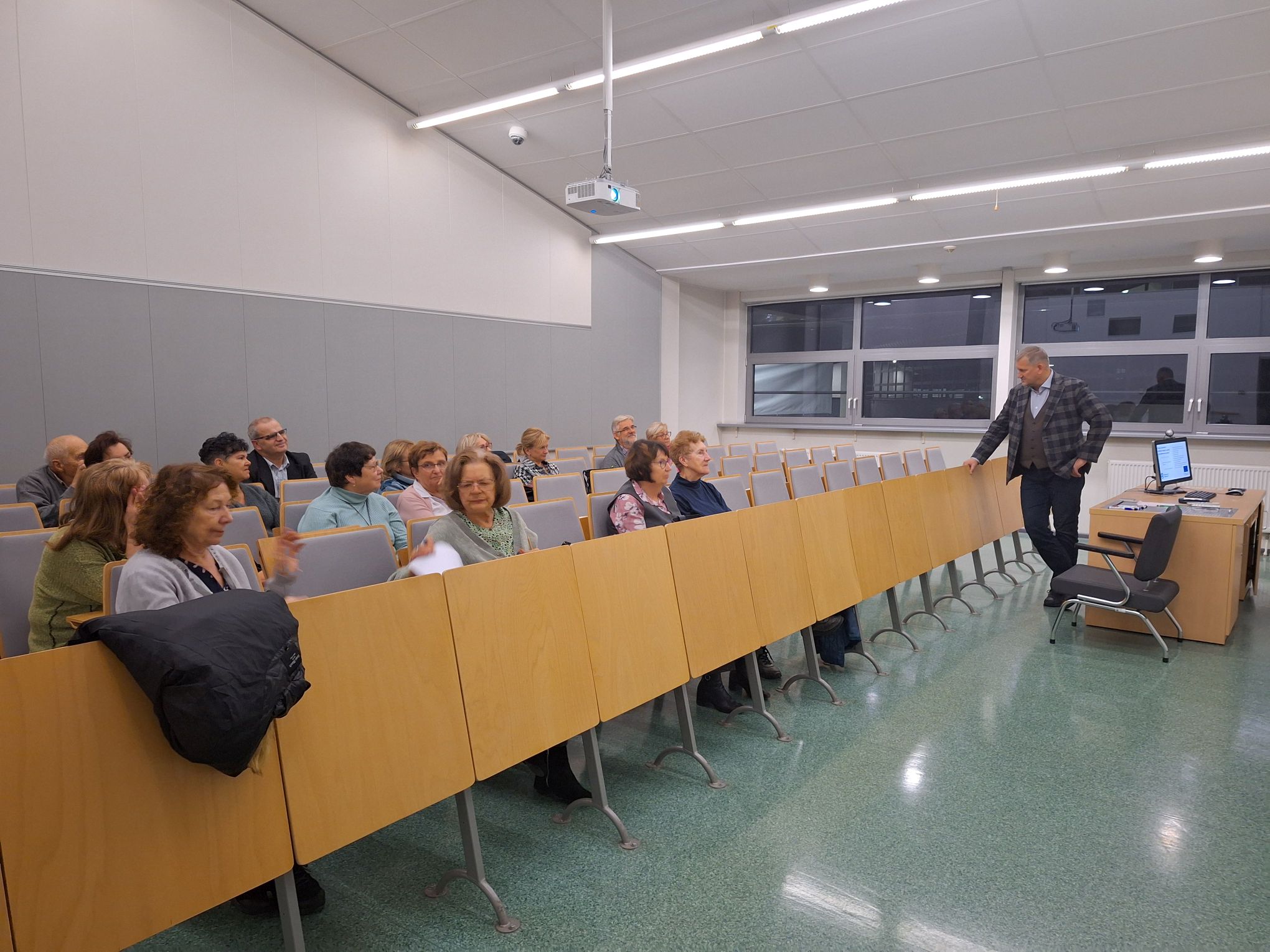 The photo shows the lecturer and the audience sitting at the lecture.